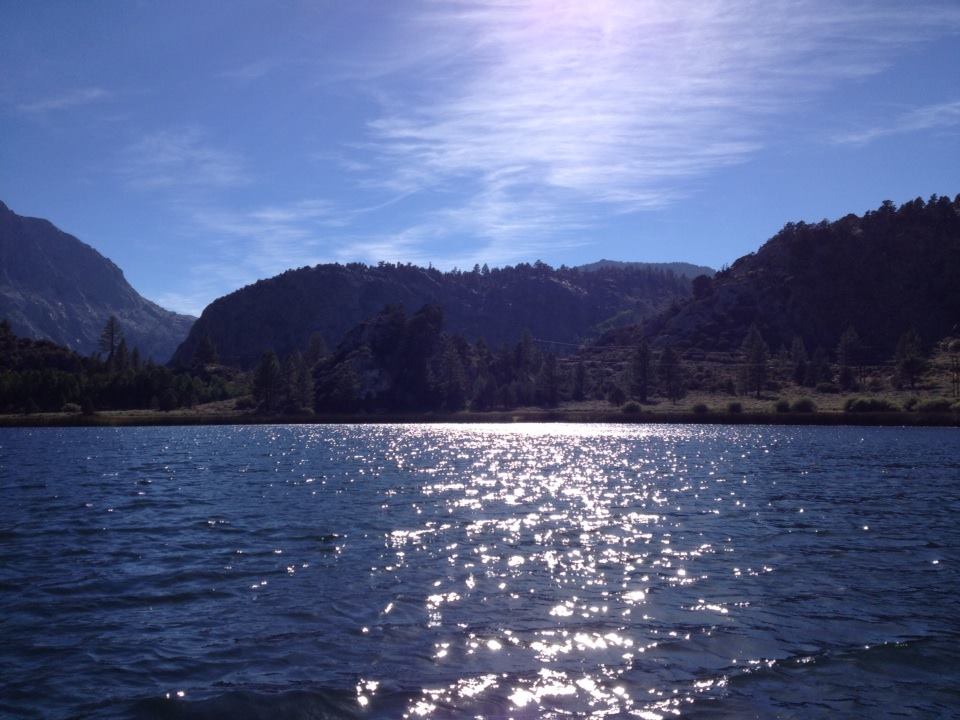 the sun shines brightly over a lake with mountains in the background
