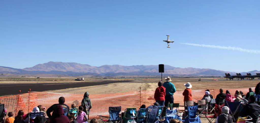 a crowd of people watching a plane fly over a runway