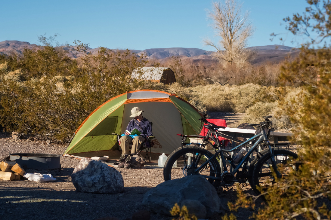 a man sits in front of his tent with his bike