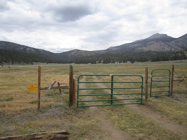 a gate in the middle of a field with mountains in the background