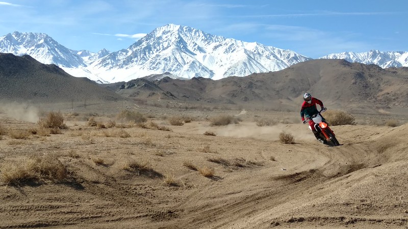 Motorcycle racing across desert blow snow-capped mountain